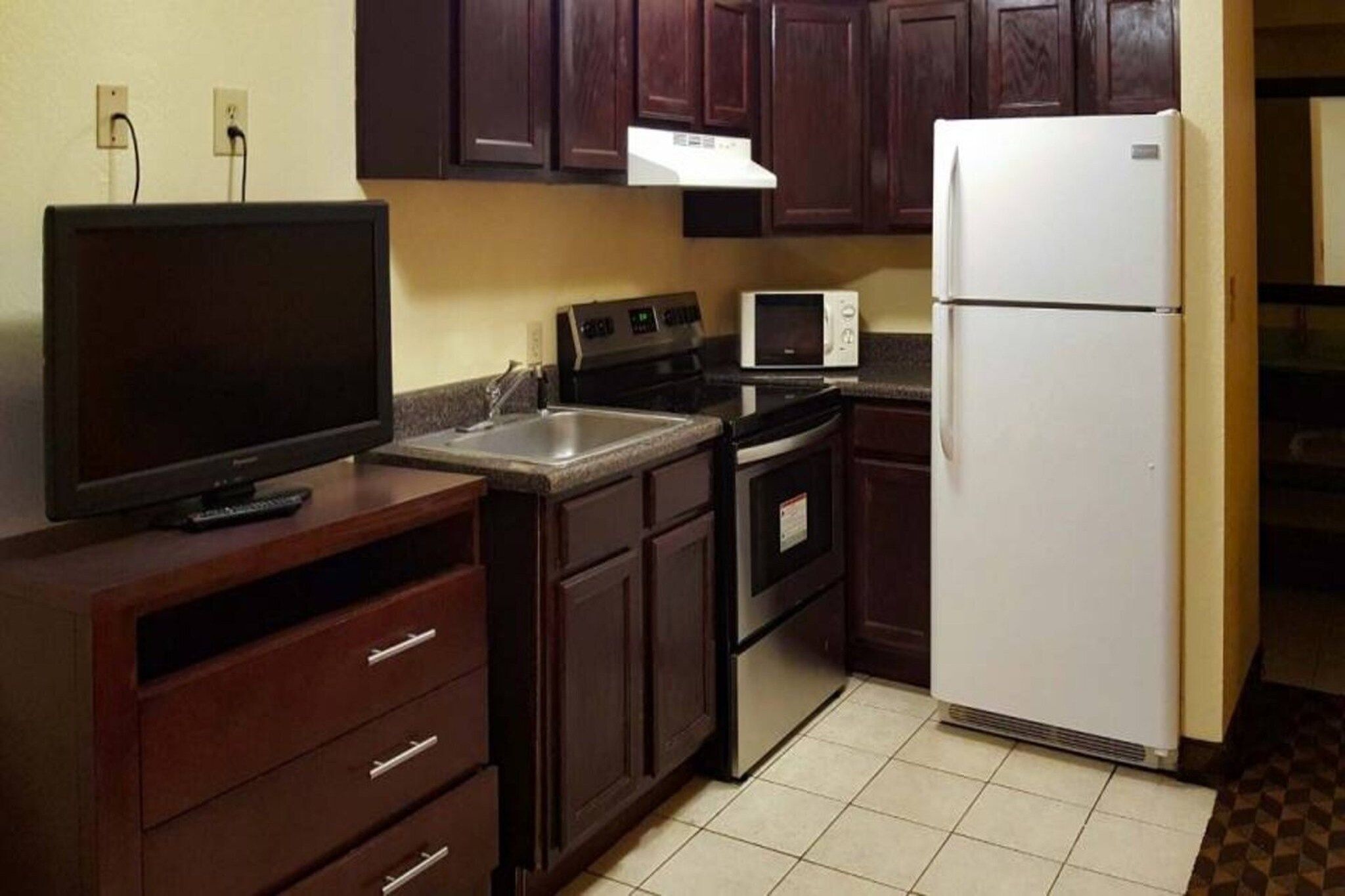 Cocina funcional con refrigerador, microondas, estufa y televisor sobre un mueble.