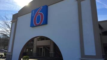 A motel entrance with a large '6' sign, an arched doorway, and a covered parking area.