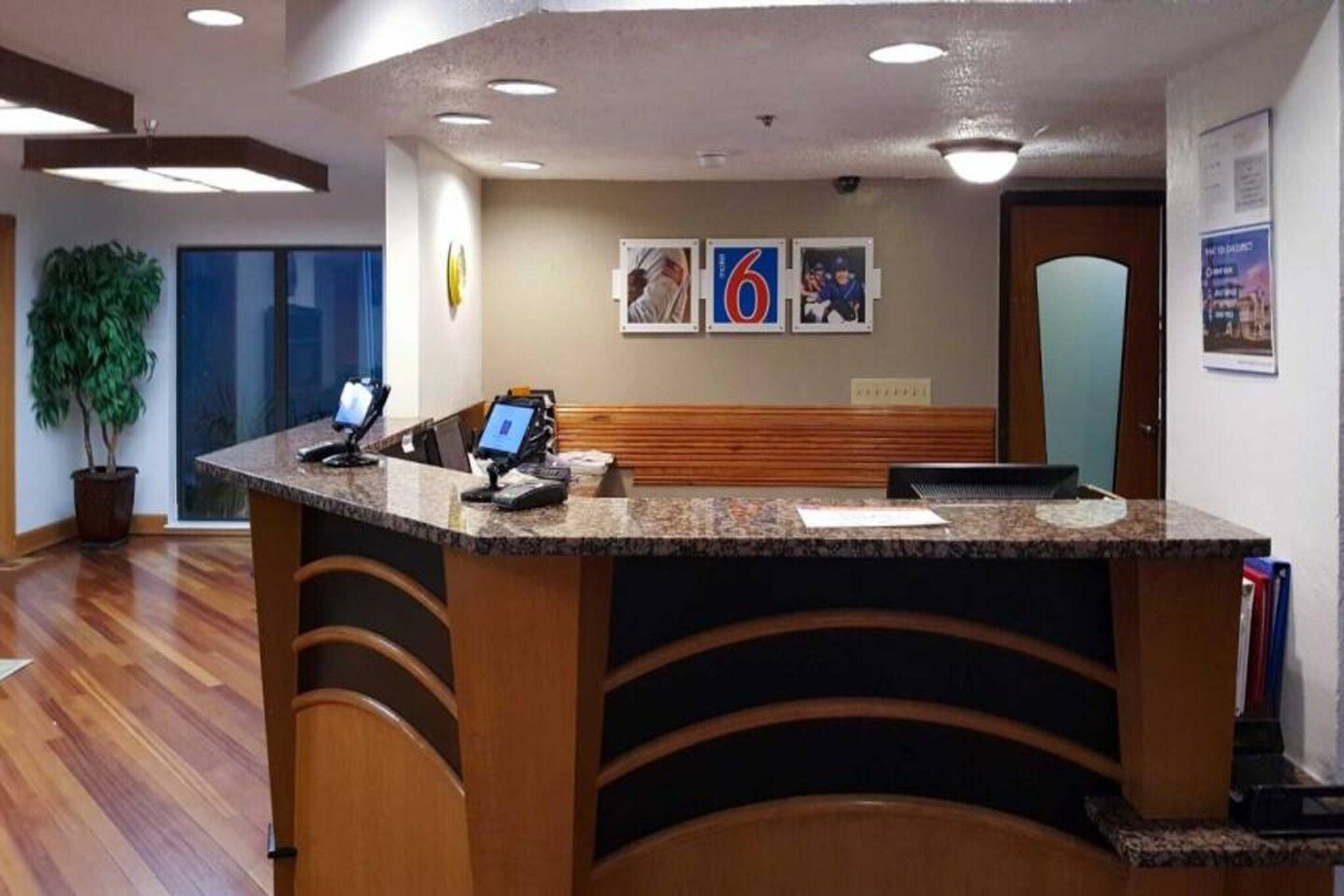 A reception desk with a computer, a phone, and a small plant. There are framed pictures on the wall and a door in the background.