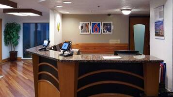 A reception desk with a computer, a phone, and a small plant. There are framed pictures on the wall and a door in the background.