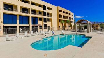 A hotel with a swimming pool, multiple balconies, and a clear blue sky.