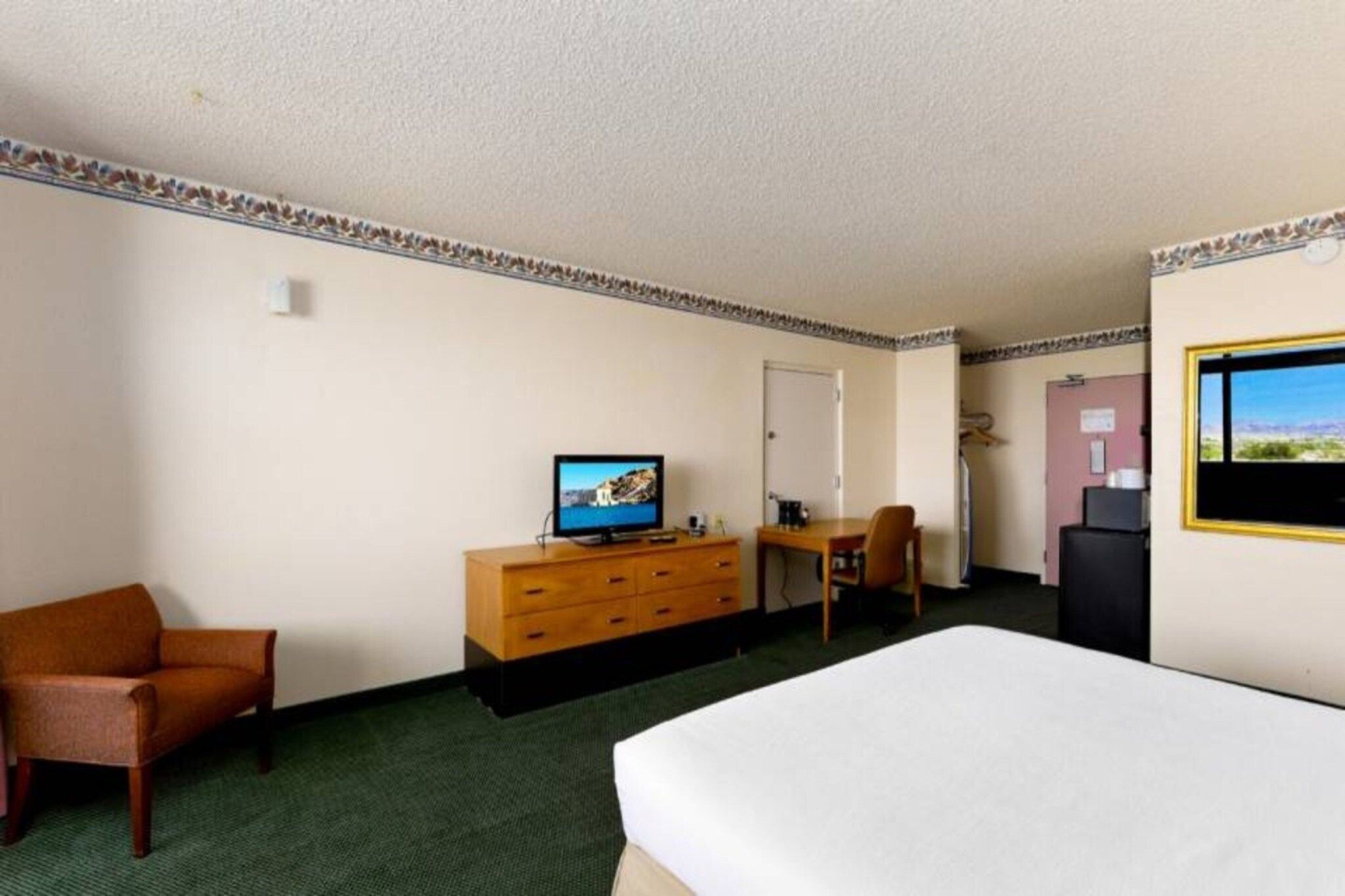 A hotel room with a bed, a desk, a chair, a dresser, a television, and a window.