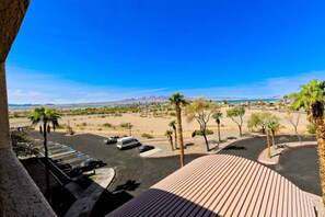 Ein Parkplatz mit Fahrzeugen, einer Holzdielen-Terrasse und Blick auf eine Wüstenlandschaft mit Palmen und fernen Bergen.