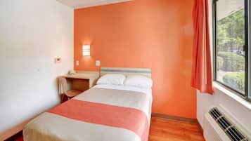 A hotel room with a bed, a desk, a window with curtains, and a radiator.