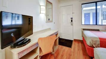 A hotel room with a television, a desk, a chair, a bed, a door, and a window.