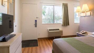 Une chambre d’hôtel comprenant un lit, un bureau avec une télévision, une fenêtre avec des rideaux, un appareil de climatisation et une porte.