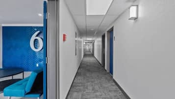 A hotel corridor with a long hallway, doors on both sides, and a blue seating area with a number '6' sign.