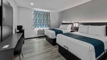 A hotel room with two beds, a desk, a TV, and a window with patterned curtains.