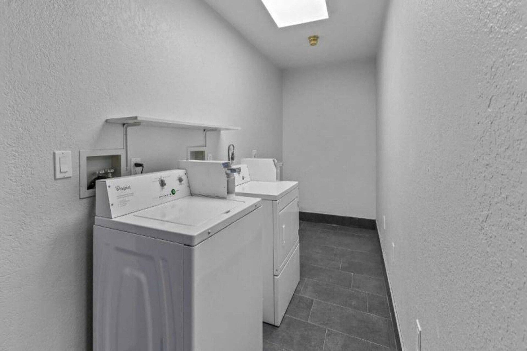A laundry room with a front-loading washer and dryer, a small sink, and a tiled floor.