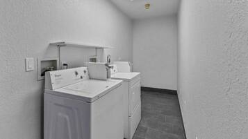 A laundry room with a front-loading washer and dryer, a small sink, and a tiled floor.