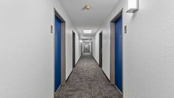 A long, narrow hotel corridor with blue doors on both sides and a carpeted floor.
