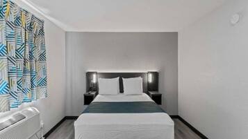 A hotel room with a bed, bedside tables, a wall-mounted heater, and a patterned curtain.