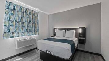 A hotel room with a bed, a wall-mounted heater, and a patterned curtain.