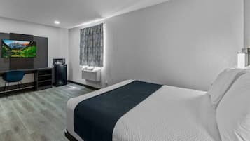 A modern hotel room with a large bed, a desk with a computer, a flat-screen TV, and a window with patterned curtains.