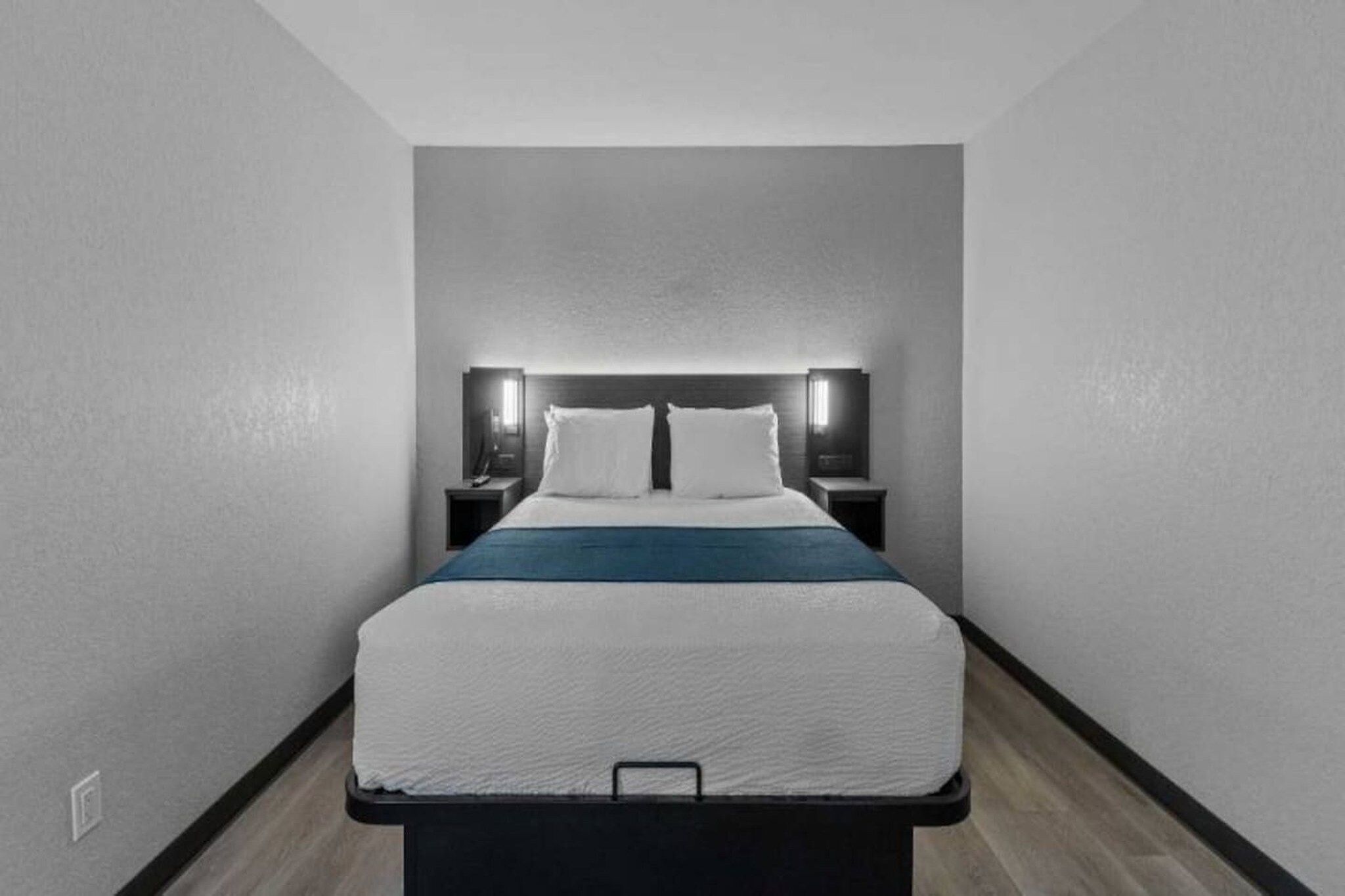 A modern hotel room with a single bed, bedside tables, and a headboard with integrated lighting.