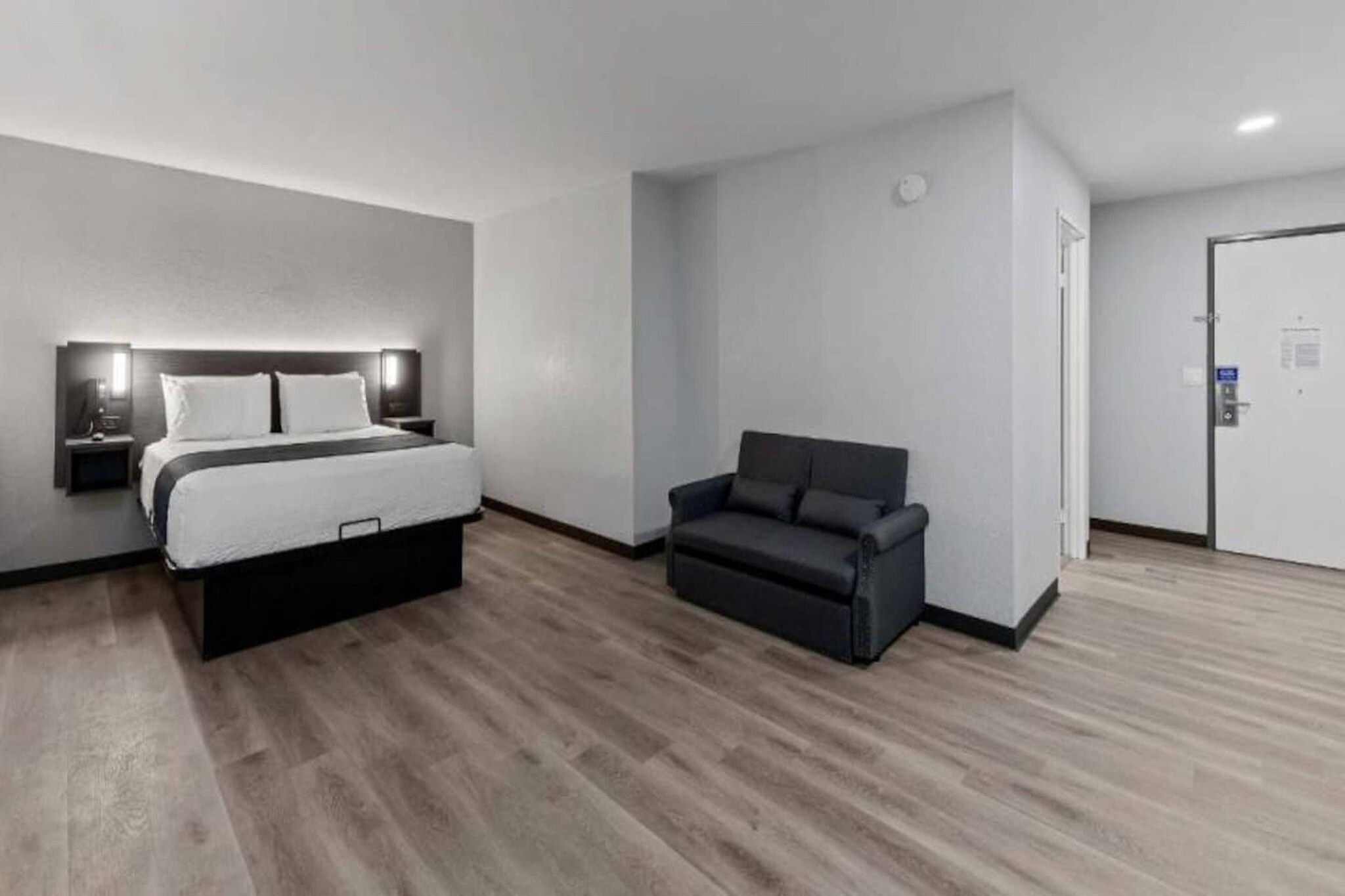 A modern hotel room with a bed, a sofa, and a door.