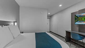 A hotel room with a bed, a desk, a chair, and a television on the wall.