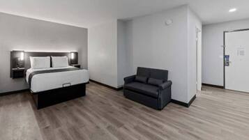 A modern hotel room with a bed, a sofa, and a door.
