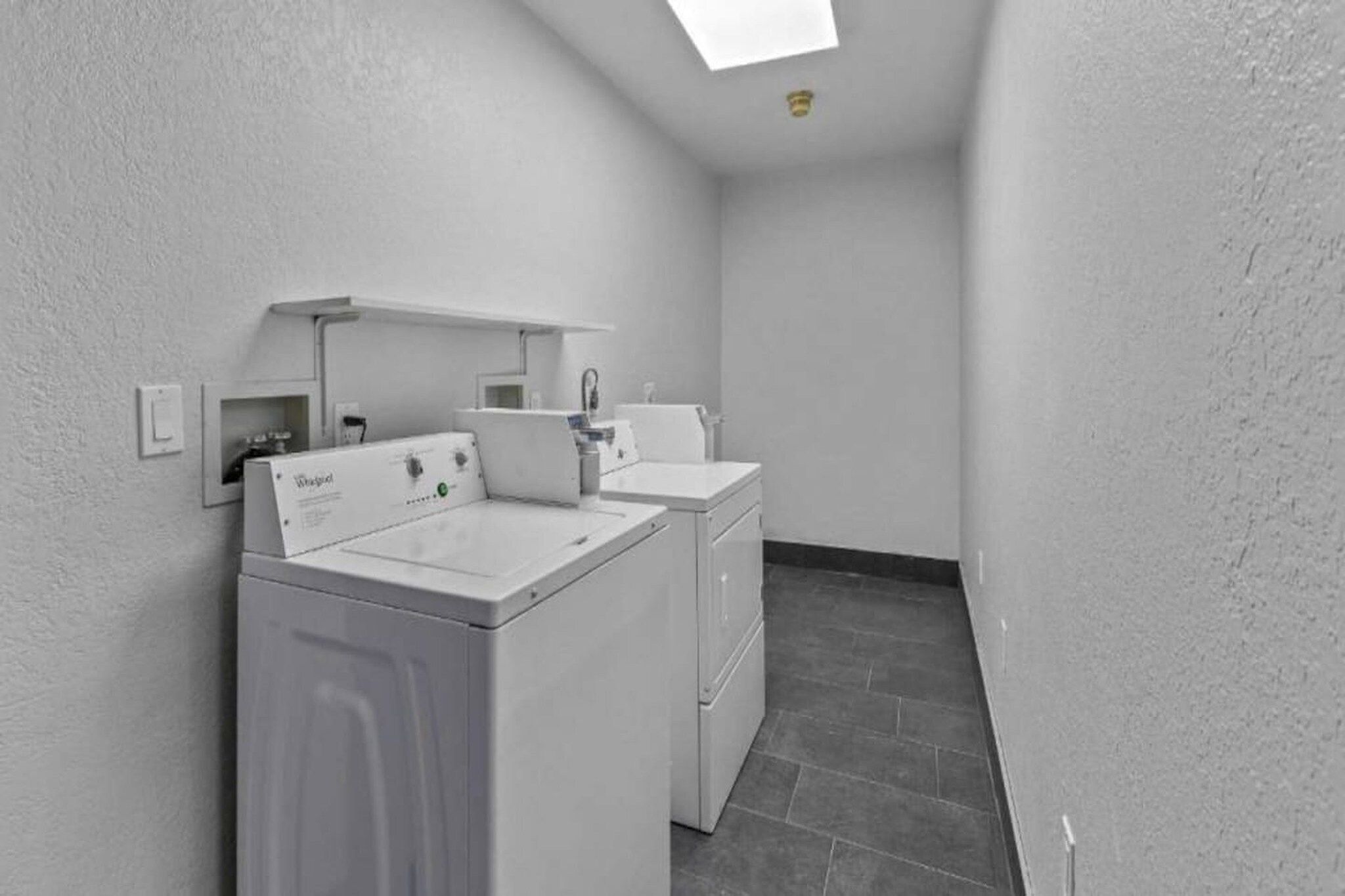 A laundry room with a front-loading washer and dryer, a small sink, and a tiled floor.