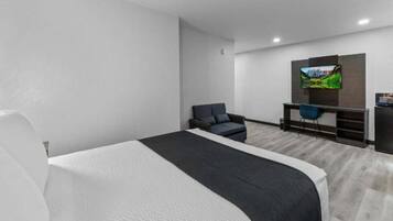 Ein modernes Hotelzimmer mit einem großen Bett, einem Schreibtisch mit Stuhl, einem an der Wand befestigten Fernseher und einer kleinen Küchenzeile.