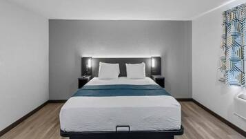 A hotel room with a bed, bedside tables, a headboard with integrated lighting, a wall-mounted air conditioning unit, and a patterned wall decoration.