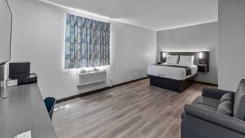 A modern hotel room with a bed, a desk, a chair, and a large window with patterned curtains.