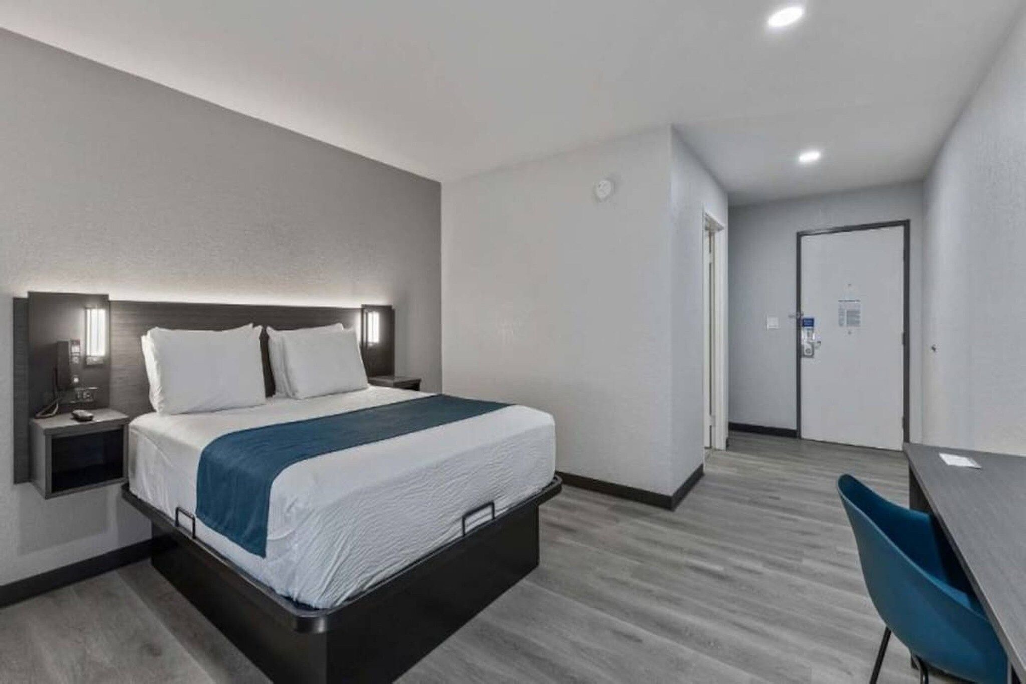 Een hotelkamer met een bed, nachtkastje en een bureau met stoel.