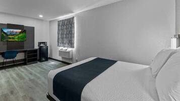 A modern hotel room with a large bed, a desk with a computer, a flat-screen TV, and a window with patterned curtains.