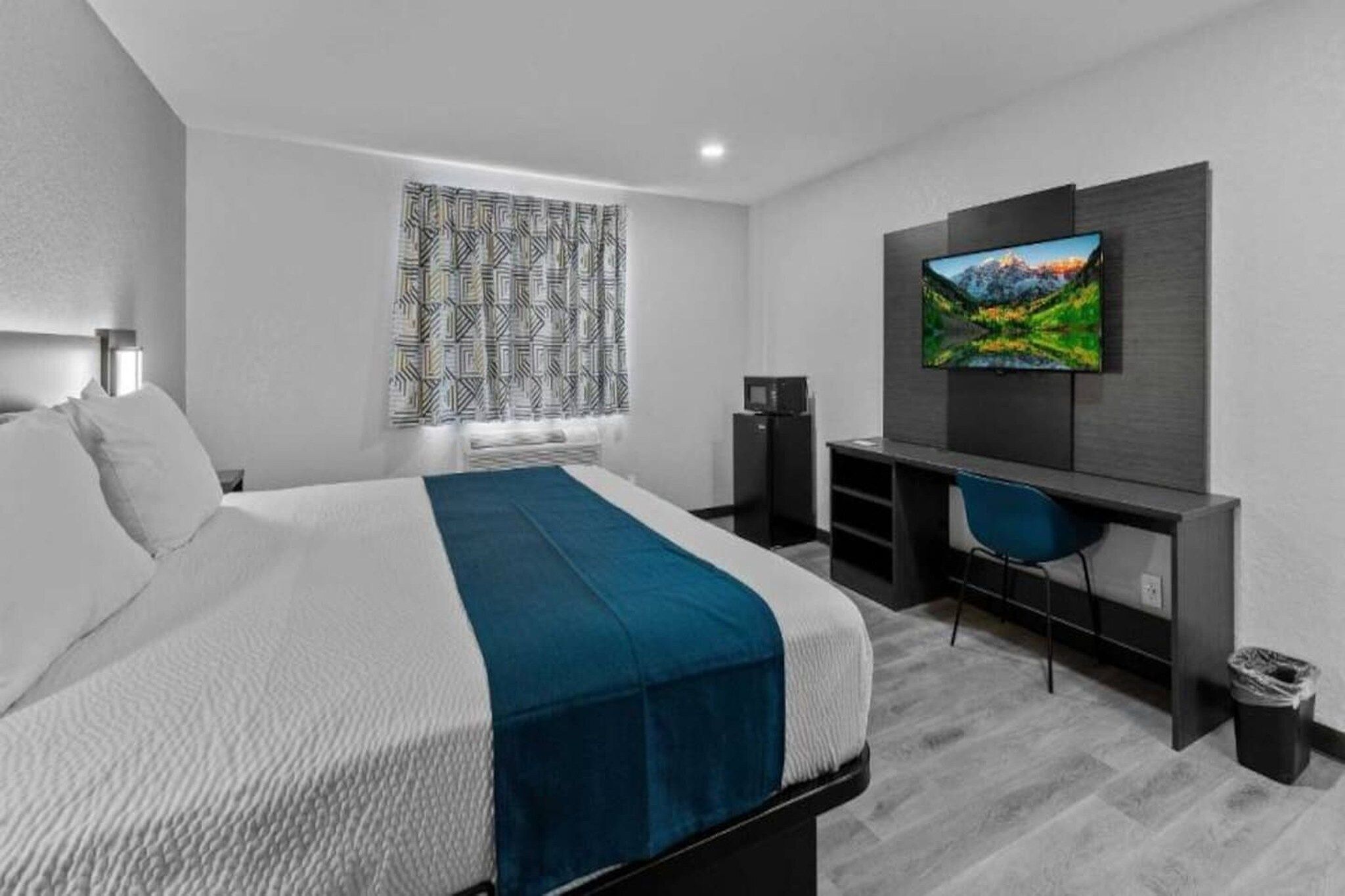Une chambre d’hôtel moderne équipée d’un lit, d’un bureau avec une chaise, d’une télévision et de rideaux à motifs.