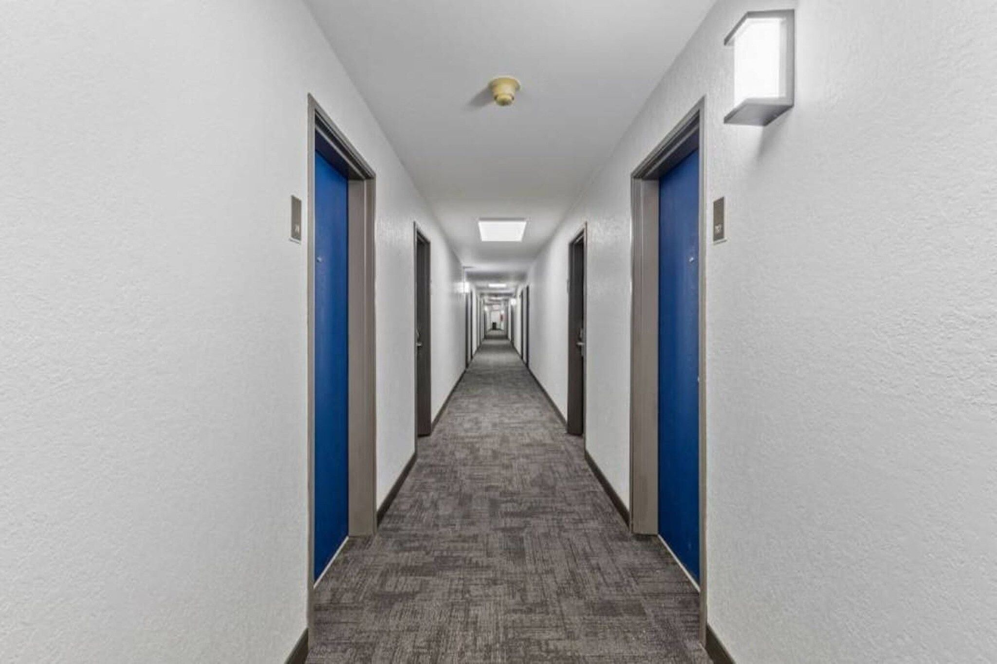 A long, narrow hotel corridor with blue doors on both sides and a carpeted floor.