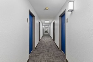 A long, narrow hotel corridor with blue doors on both sides and a carpeted floor. - 1 King Bed | Non-Smoking, Micfridge (Brighton CO)