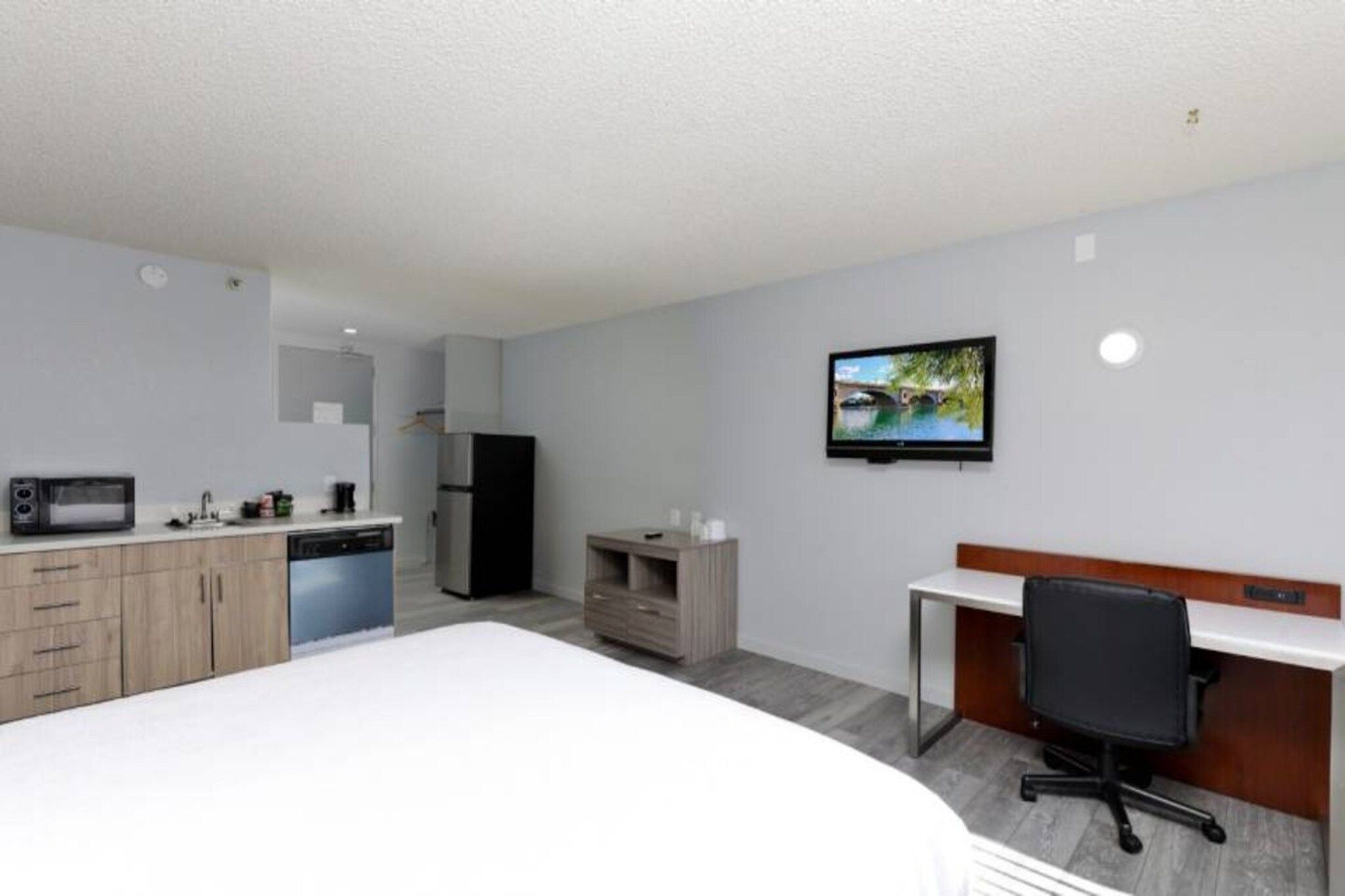 A hotel room with a bed, a desk, a chair, a television, a microwave, a refrigerator, and a small kitchenette.