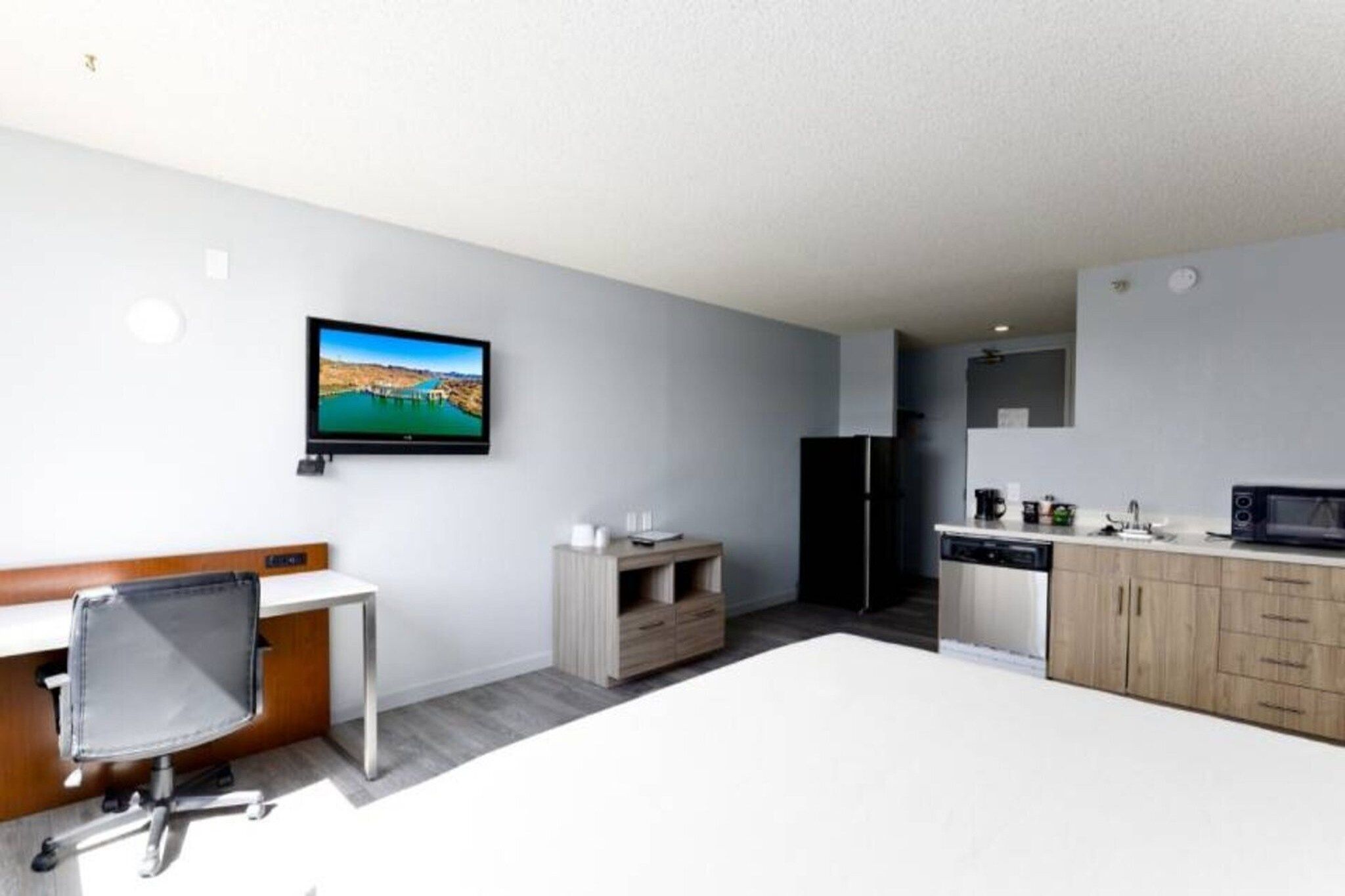A modern kitchen with a flat-screen TV, wooden cabinets, and a dining area with a white table and chair.