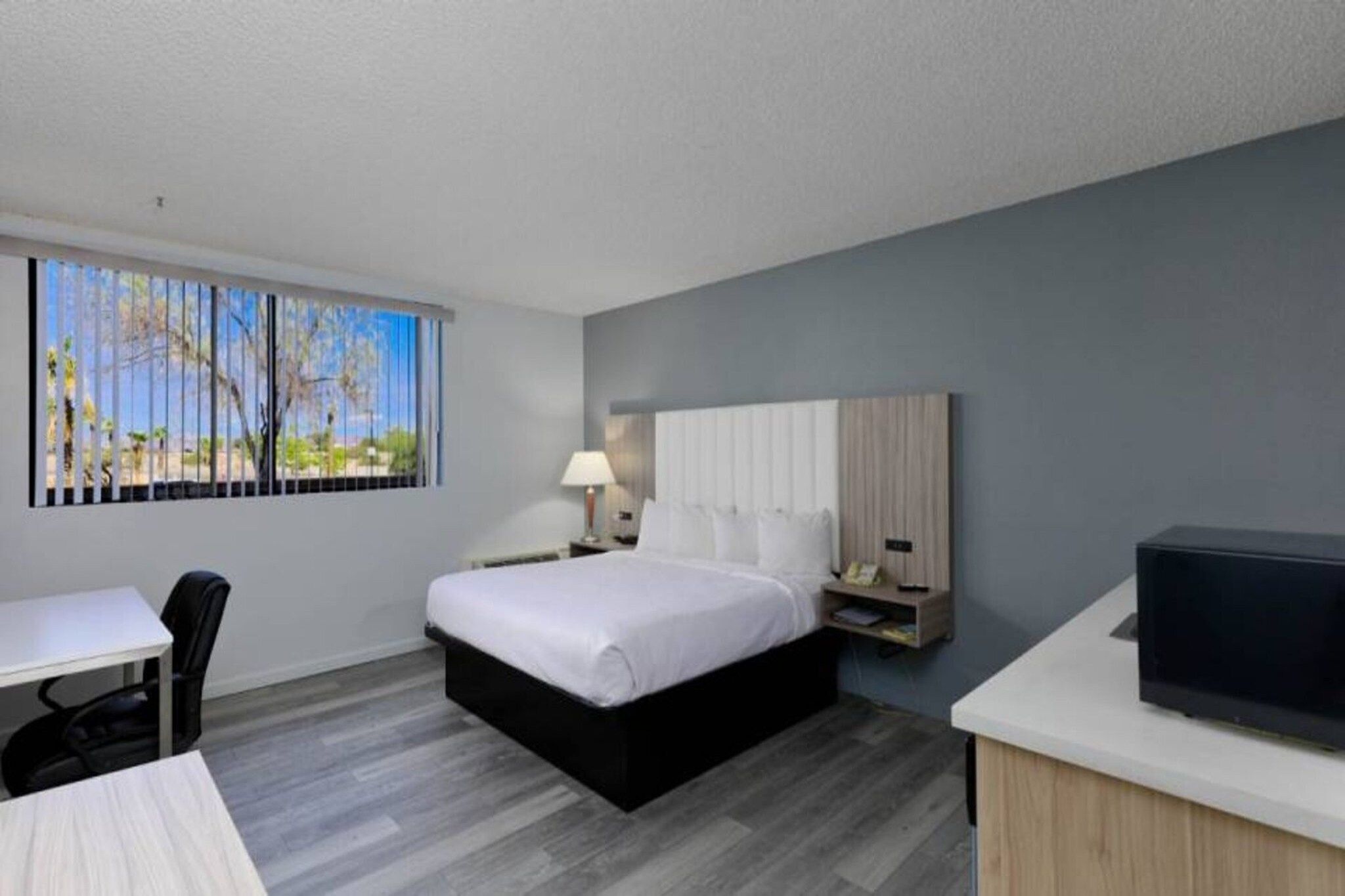 A hotel room with a bed, a desk, a chair, a TV, and a window with a view.