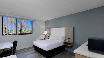 A hotel room with a bed, a desk, a chair, a TV, and a window with a view.