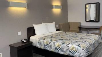 Ein Hotelzimmer mit Bett, Nachttisch, Stuhl und einem kleinen Tisch mit Spiegel.