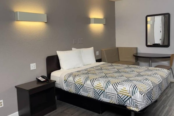 A hotel room with a bed, bedside table, chair, and a small table with a mirror.