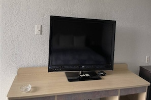 A flat-screen TV on a wooden desk with a remote control and a small decorative item.