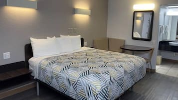 A hotel room with a bed, a desk, a chair, a mirror, and a small table.