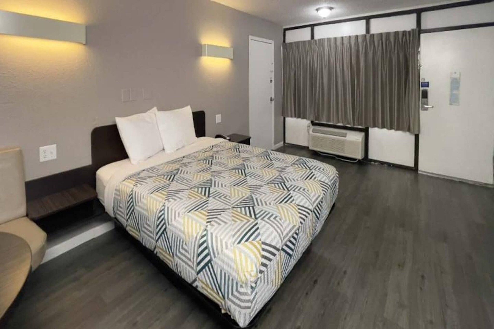 Hotellihuone, jossa on sänky, sohva, työpöytä, ikkuna verhoilla ja seinään kiinnitetty lämmitin.