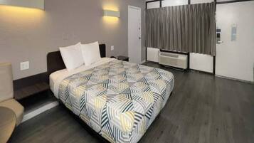 Hotellihuone, jossa on sänky, sohva, työpöytä, ikkuna verhoilla ja seinään kiinnitetty lämmitin.