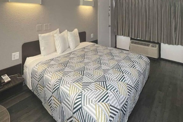 A hotel room with a bed, a bedside table, a lamp, and a window with curtains.