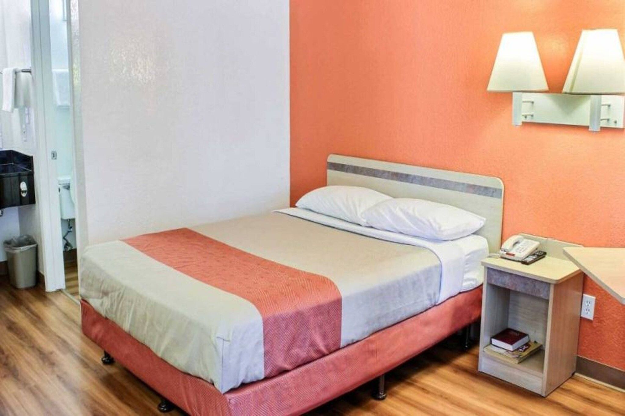 A hotel room with a bed, a nightstand, a lamp, and a trash bin.
