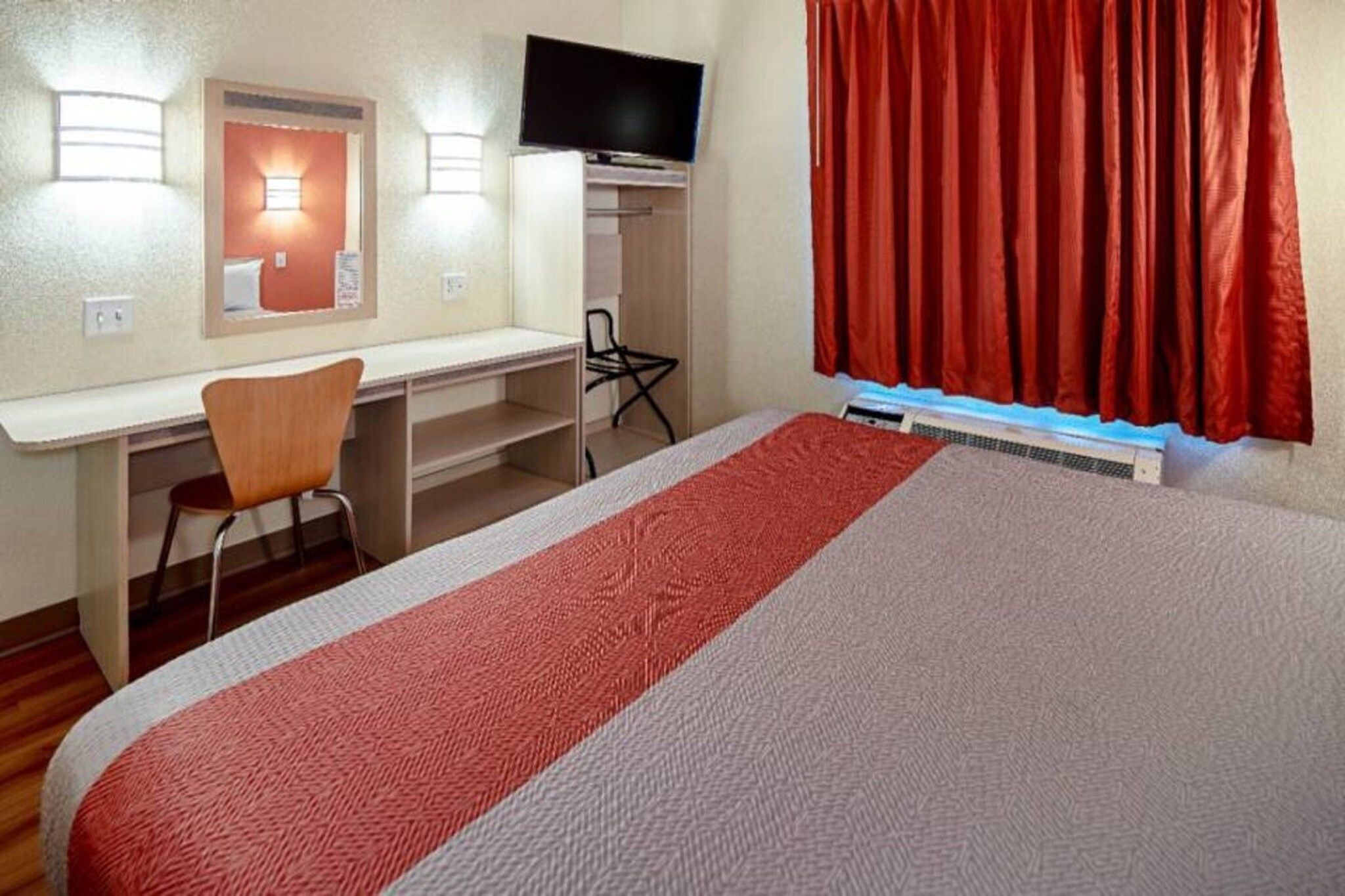 Une chambre d’hôtel équipée d’un lit, d’un bureau, d’une chaise, d’une télévision et d’une fenêtre avec des rideaux.