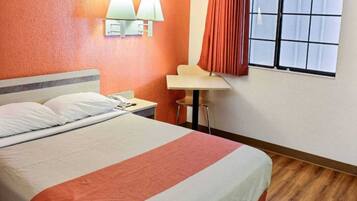Een hotelkamer met een bed, een bureau, twee wandlampen en een raam met gordijnen.