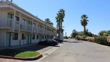 A row of motel buildings with balconies, parked cars, and palm trees.
