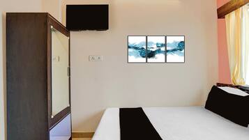 Una habitación de hotel con una cama, un televisor de pantalla plana montado en la pared y un conjunto de obras de arte abstracto sobre la cama.