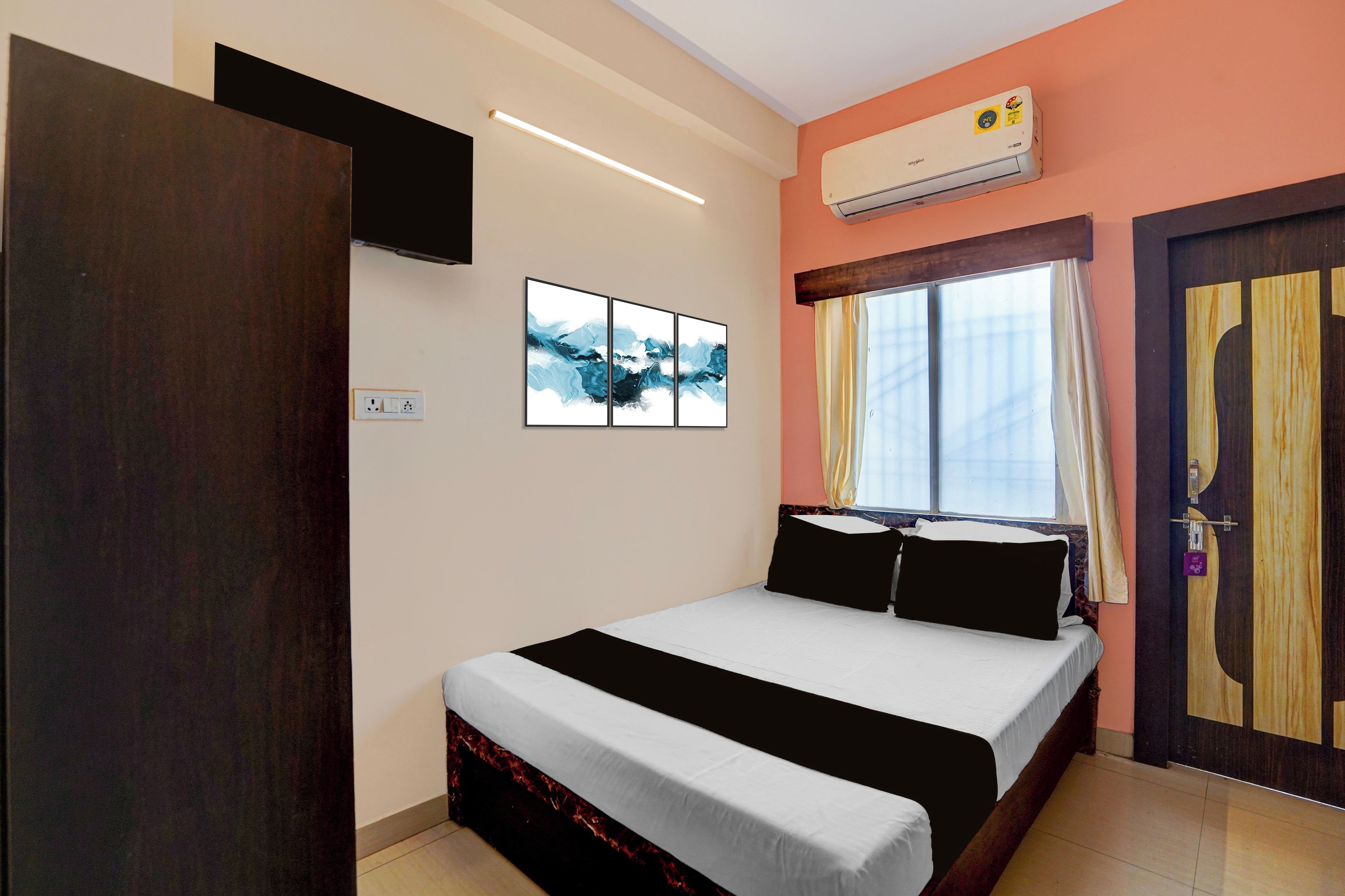Habitación de hotel con cama, televisor de pantalla plana en la pared, equipo de aire acondicionado y ventana con cortinas.