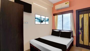 Habitación de hotel con cama, televisor de pantalla plana en la pared, equipo de aire acondicionado y ventana con cortinas.