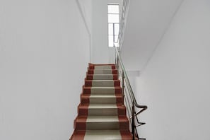 Una escalera con escalones de rojo y blanco alternados, una barandilla de metal y un ventanal en la parte superior.